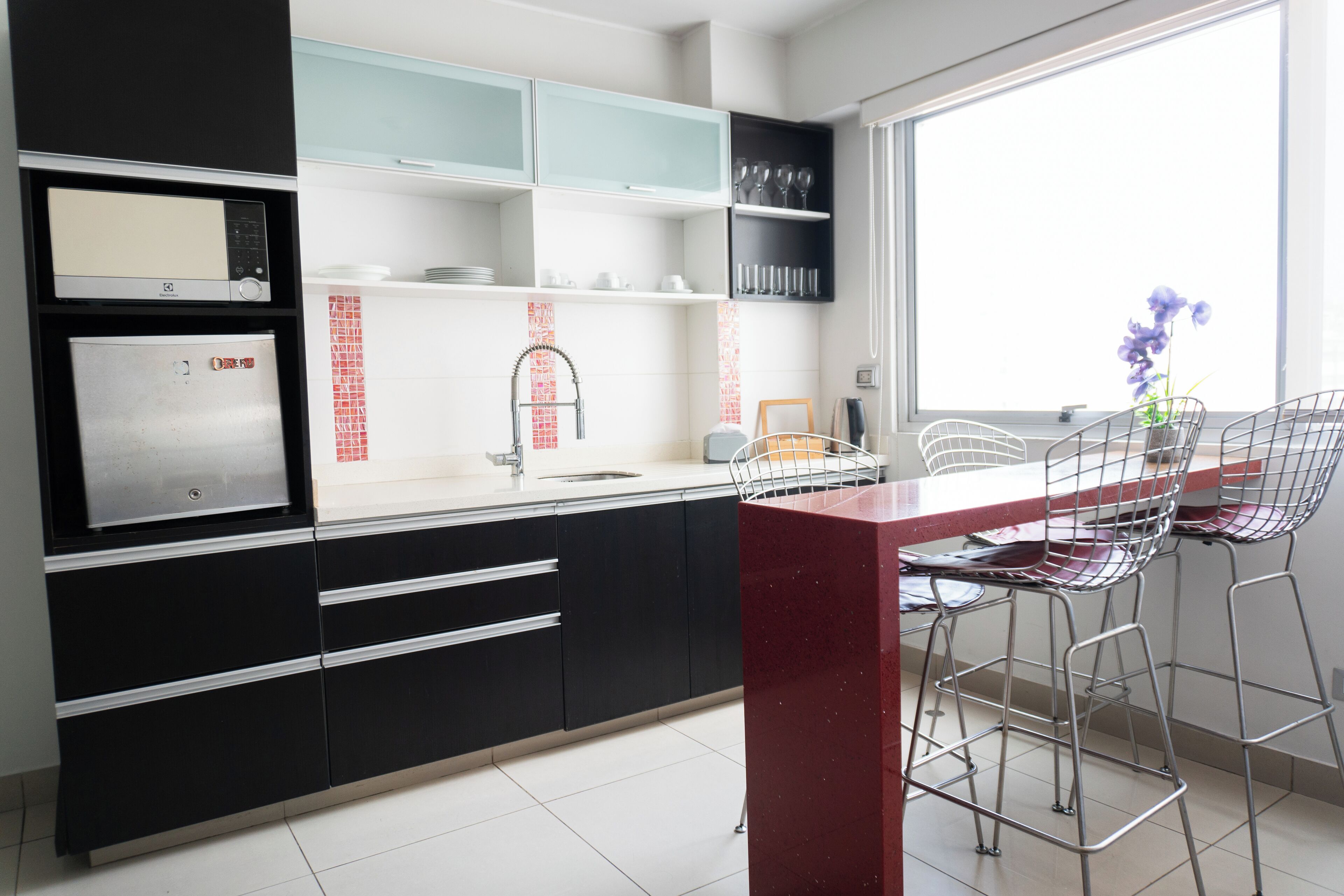 A modern kitchen with black cabinets, a stainless steel refrigerator, a red countertop, and bar stools.