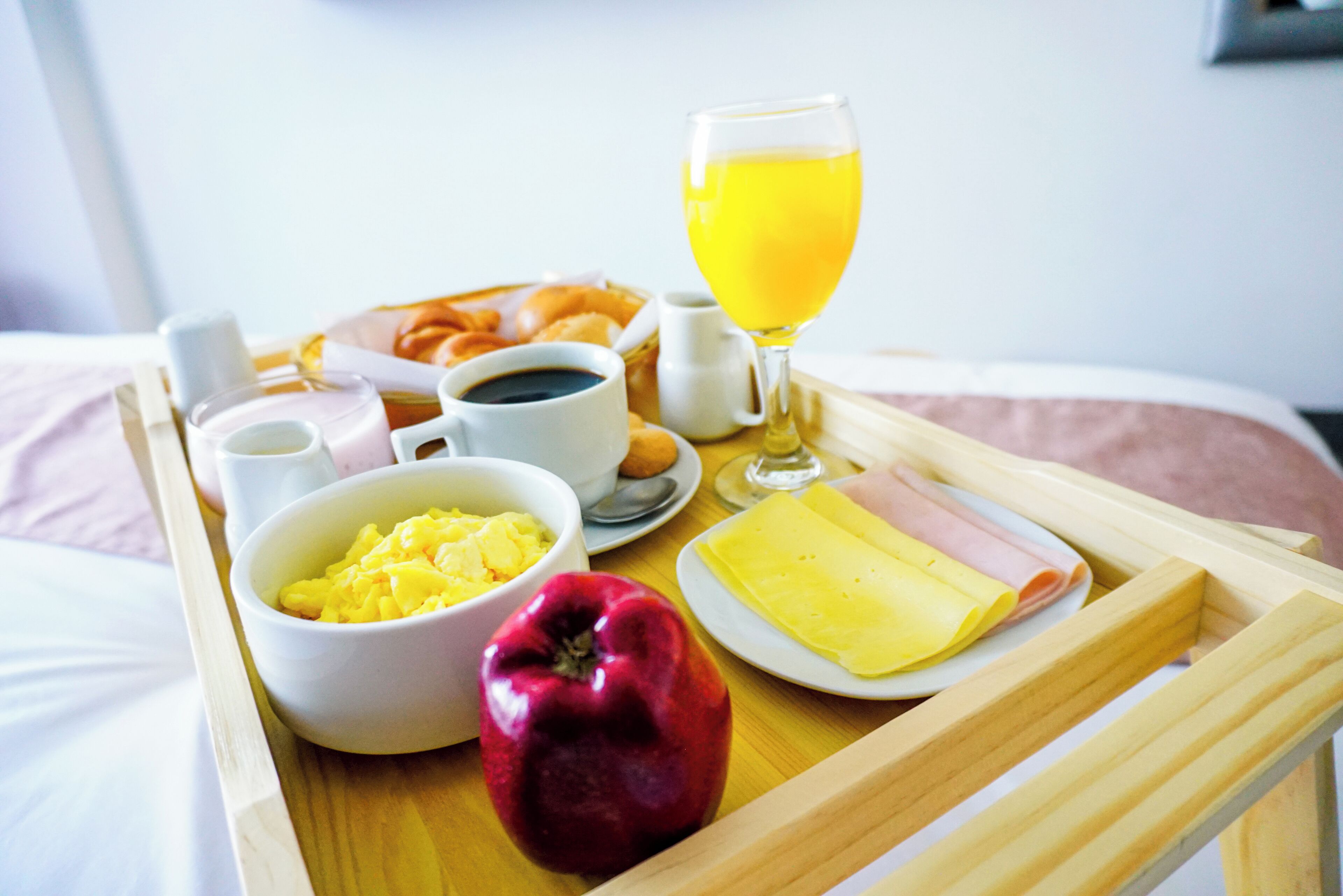 Un plateau de petit-déjeuner avec des œufs, des toasts, du jambon, un verre de jus d’orange et une pomme rouge, le tout posé sur une table.