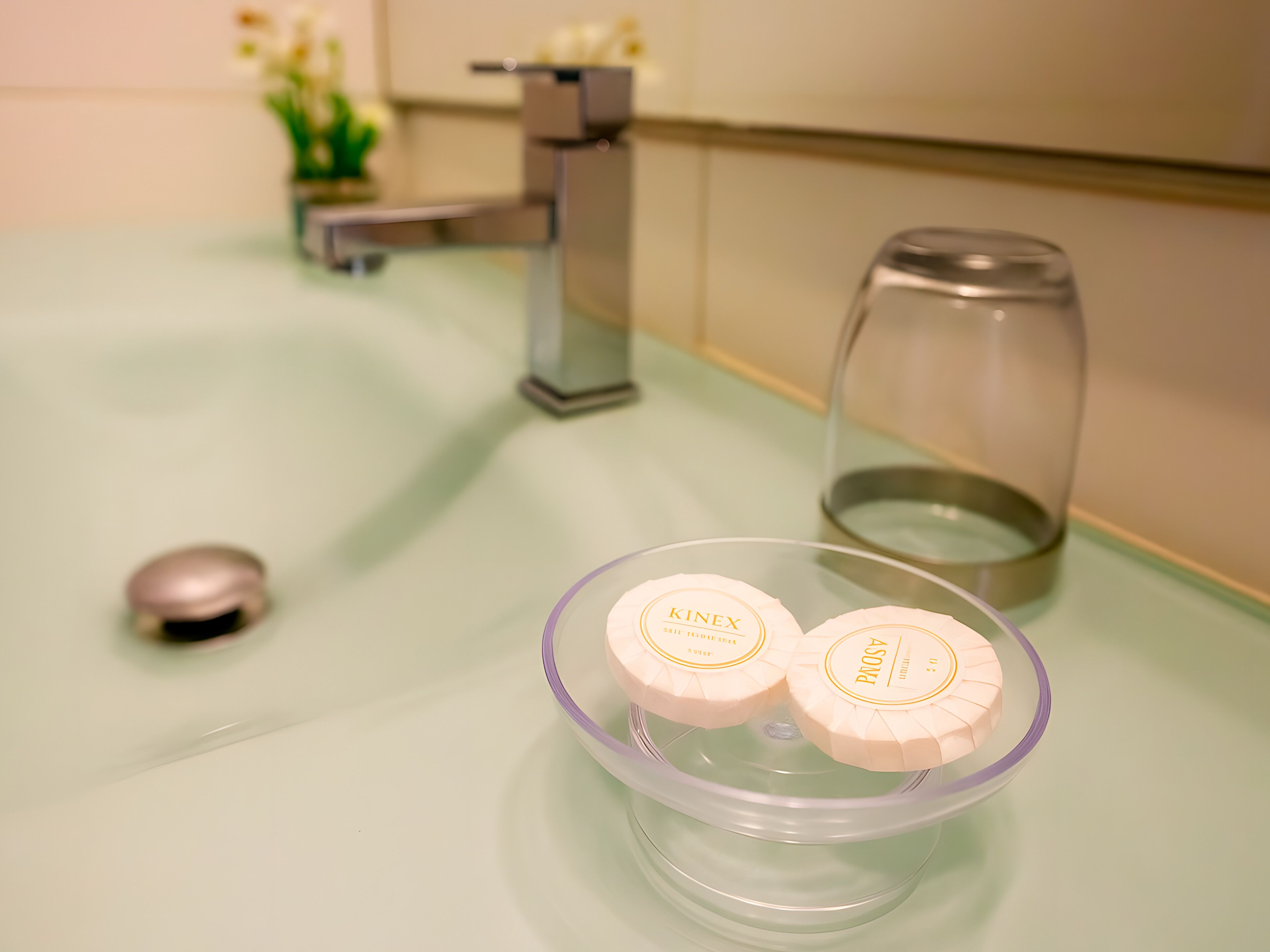A bathroom sink with a glass soap dish holding two soap bars, a faucet, and a glass container.
