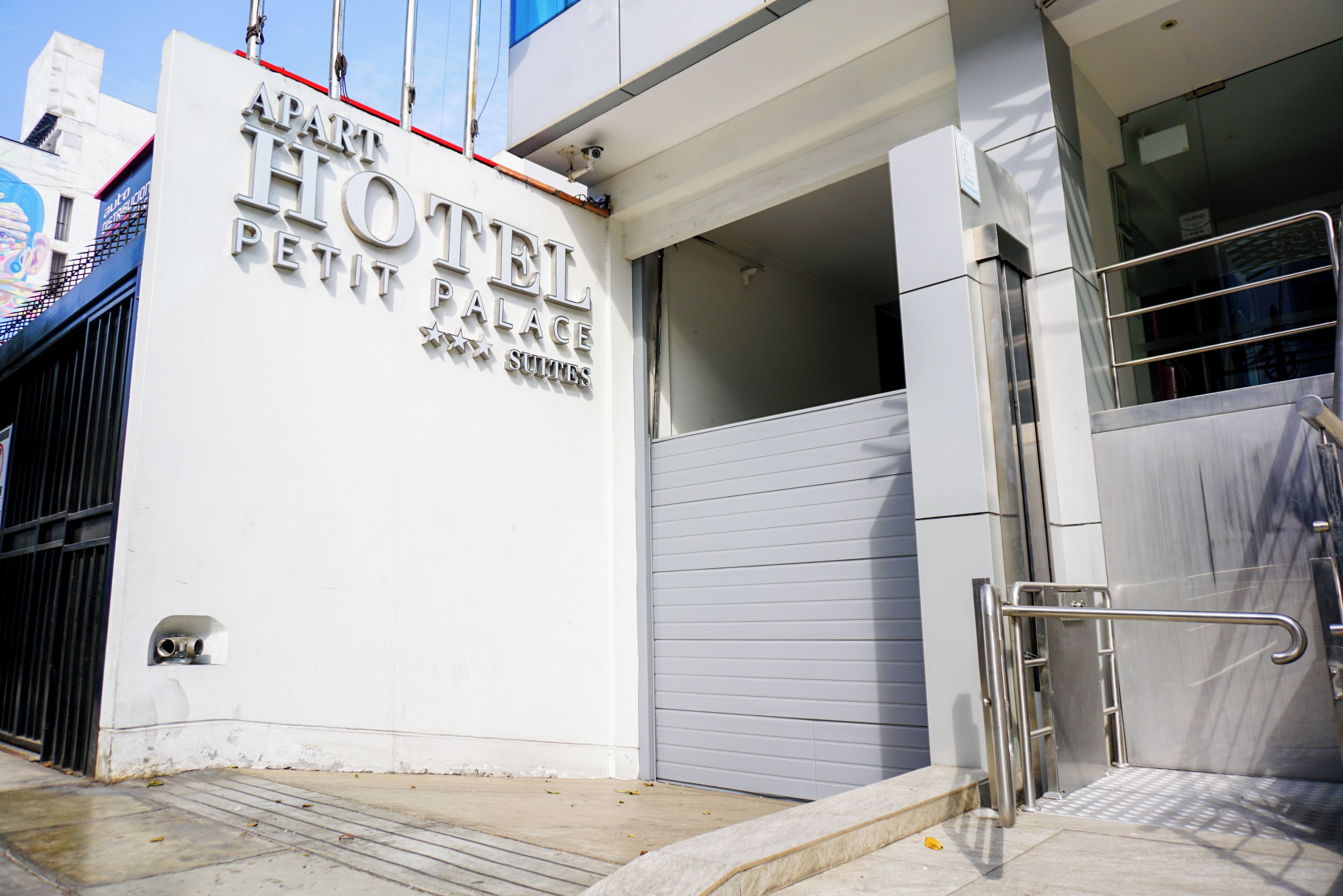 The exterior of the Apart Hotel Petit Palace with a closed grey shutter door and a metal handrail beside it.