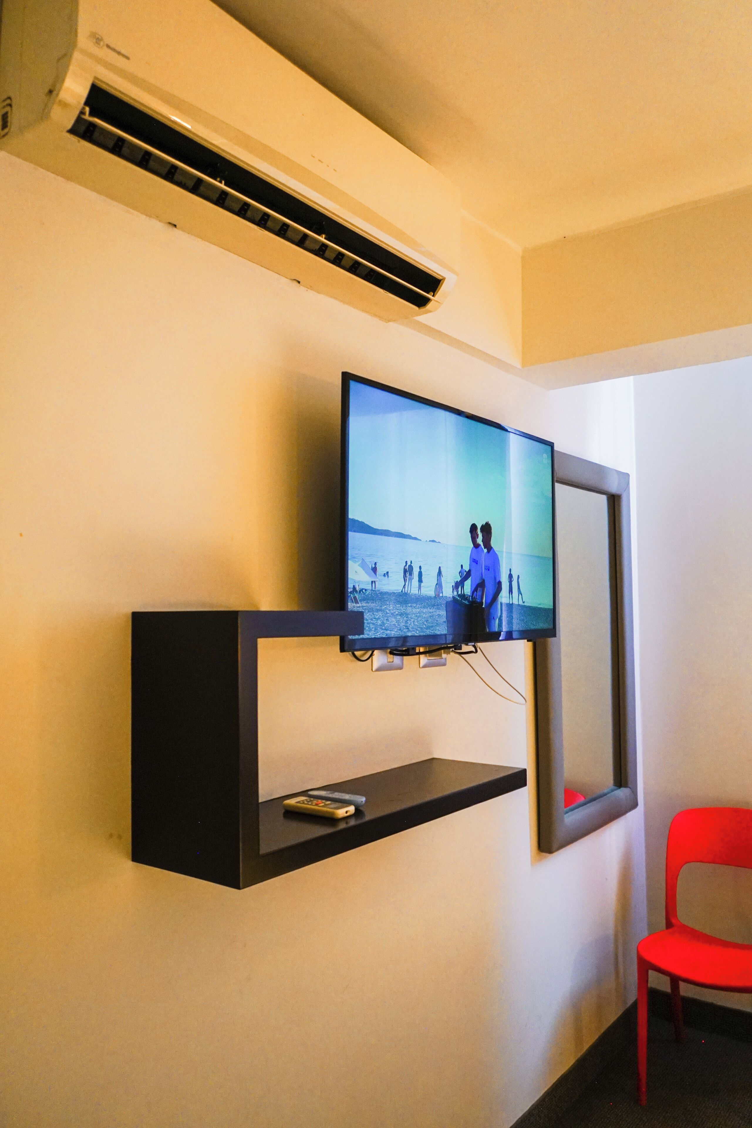 A television mounted on a wall with a remote control on a shelf below.