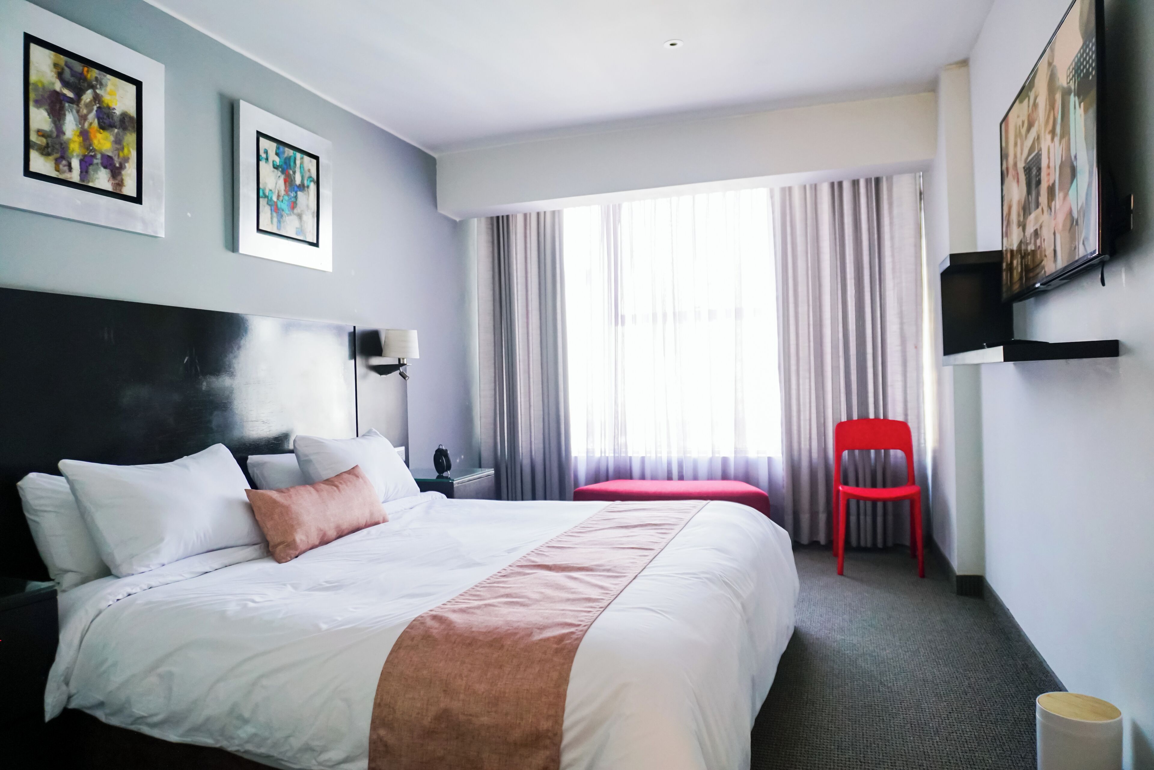 Een hotelkamer met een groot bed, een rode stoel, een flatscreen televisie en twee kunstwerken in lijsten aan de muur.