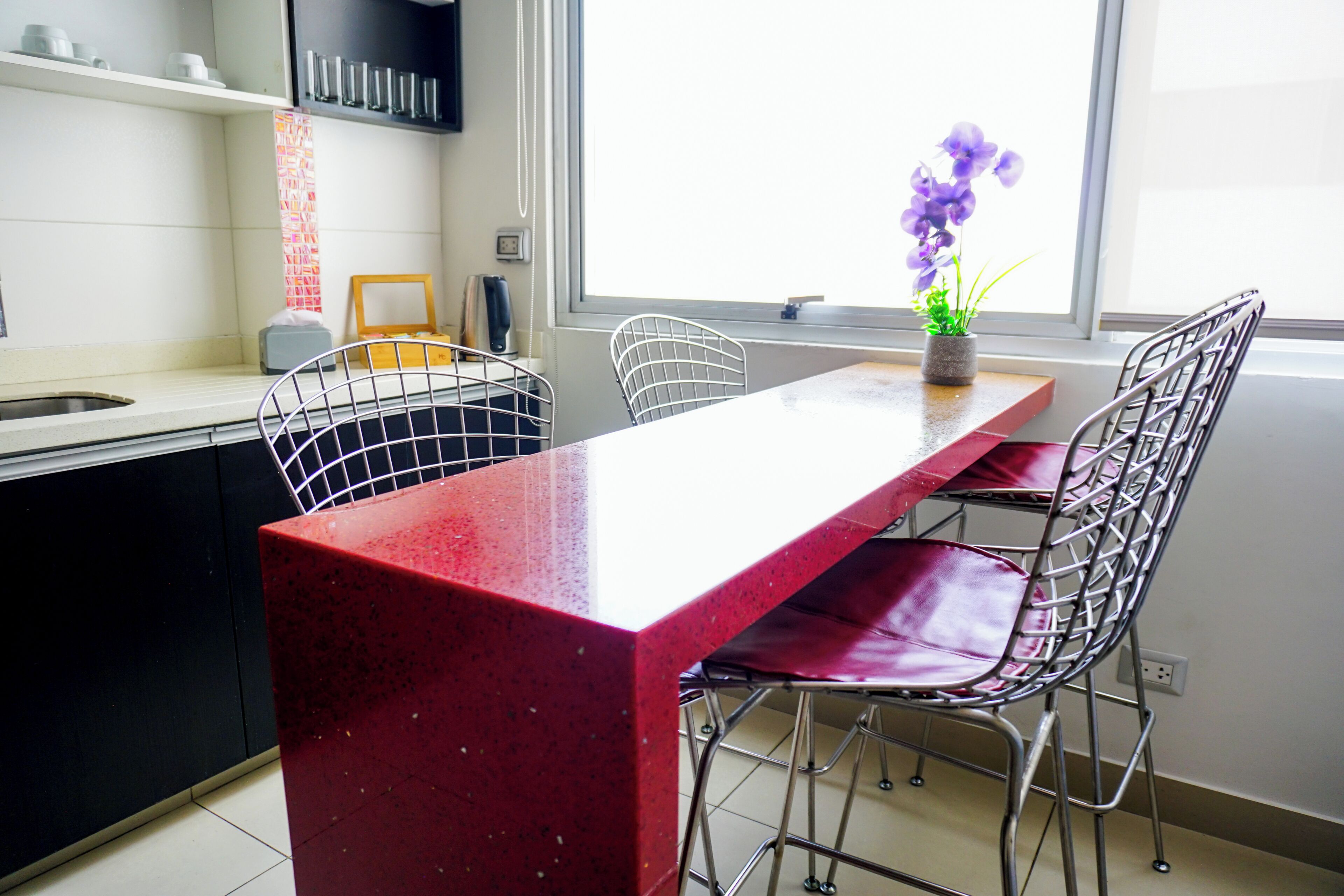 A kitchen with a red countertop, white chairs, and a window with a view.