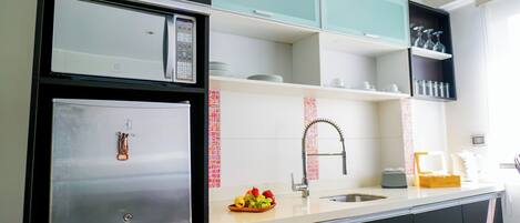 Una cocina moderna con un refrigerador de acero inoxidable, un microondas y un lavamanos con grifo. Hay armarios sobre la encimera y un frutero en la encimera.