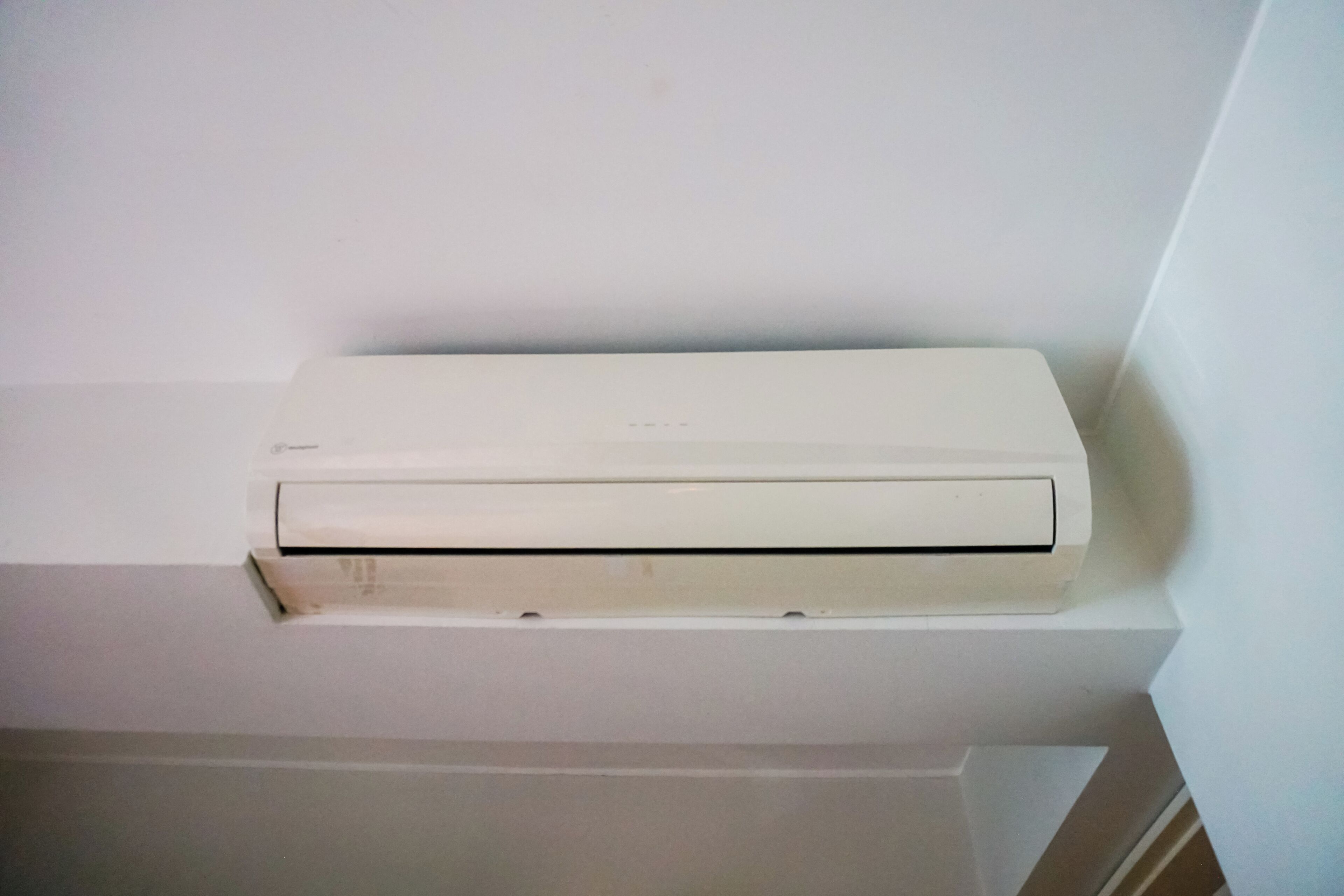 A white air conditioning unit mounted on a white wall in a corner.