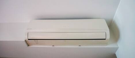 A white air conditioning unit mounted on a white wall in a corner.