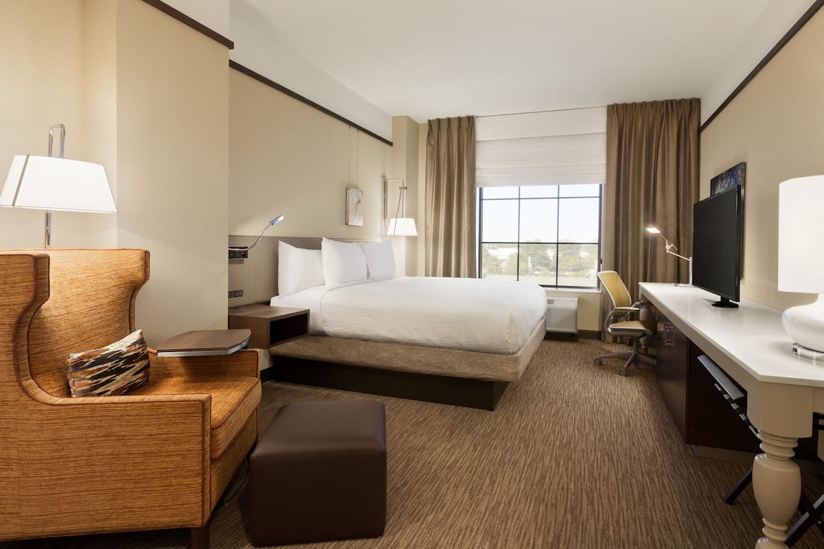 A hotel room with a large bed, a desk, a chair, a sofa, and a TV.