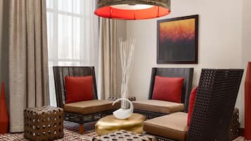 Un rincón acogedor con sillones y otomanas de mimbre, un florero decorativo y una lámpara colgante roja de gran tamaño.