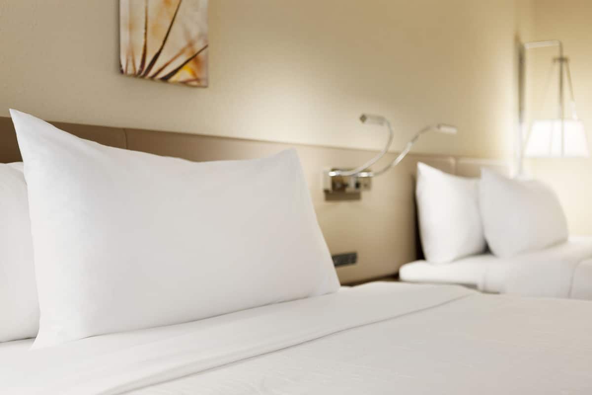 A hotel room with a neatly made bed, a bedside table, and a lamp.