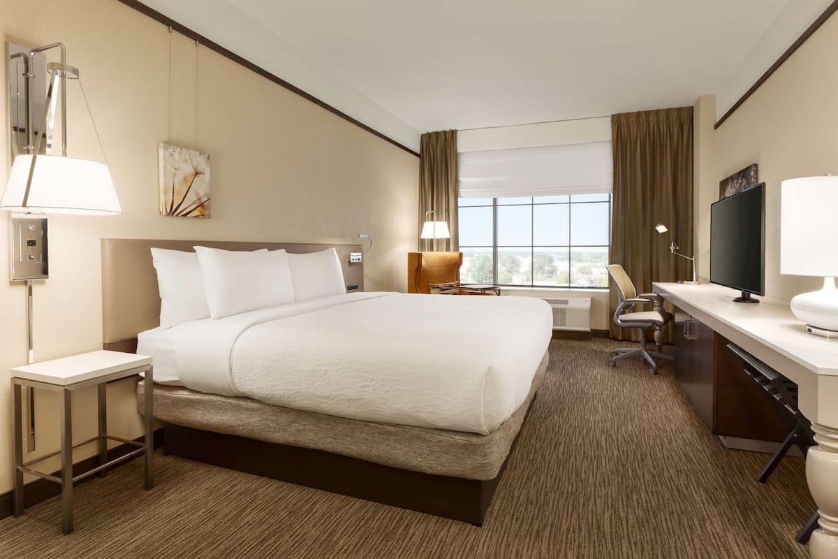 A hotel room with a large bed, a desk, a chair, a TV, and a window with curtains.