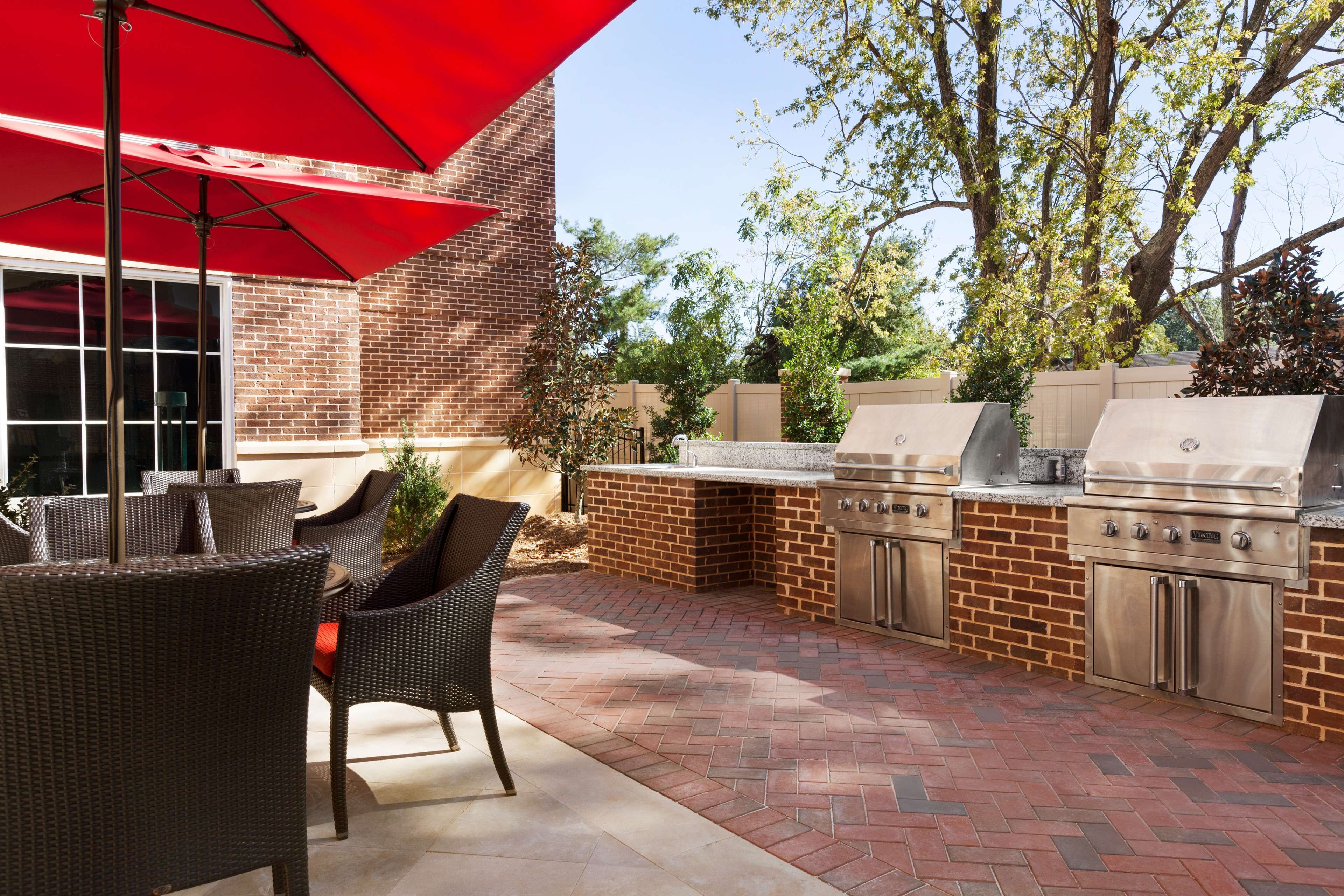 An outdoor patio with wicker furniture, a red umbrella, and a brick barbecue area with stainless steel appliances.