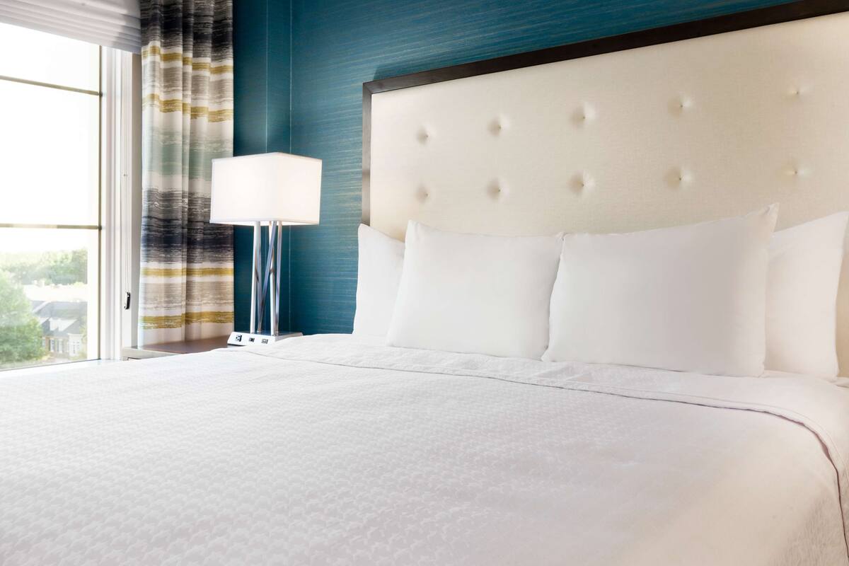 A neatly made bed with white linens, a tufted headboard, and a bedside lamp.