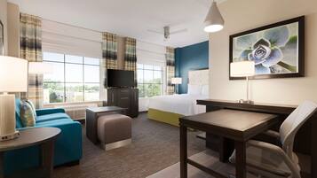 A hotel room with a bed, a desk, a chair, a sofa, a television, and a window with curtains.