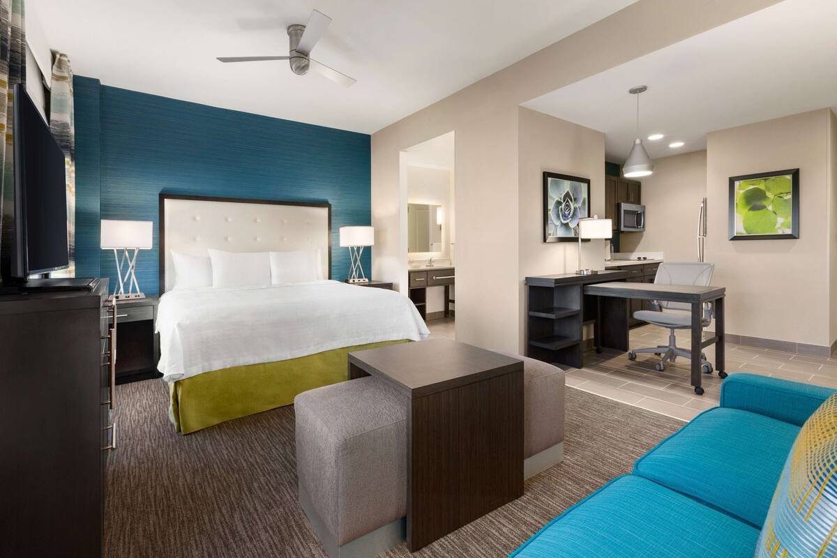 A hotel room with a bed, a desk, a chair, a sofa, and a TV.