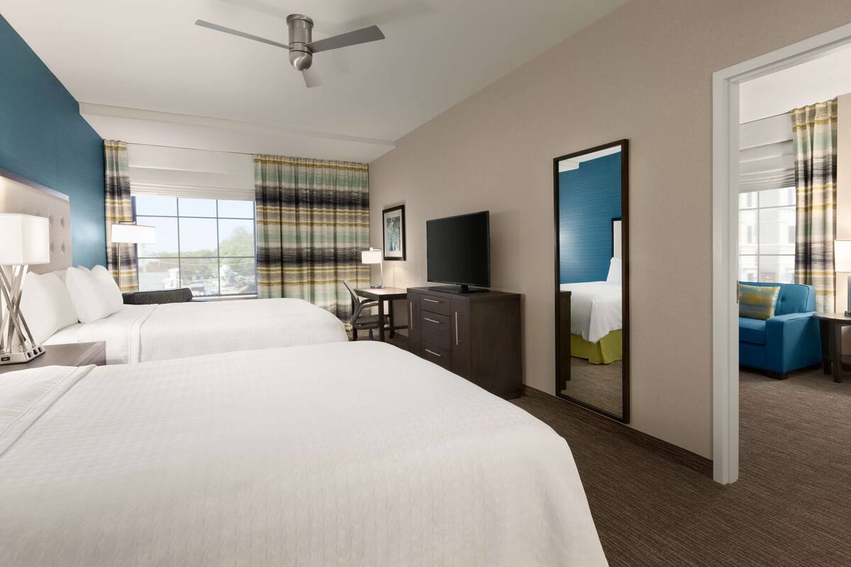 A hotel room with two beds, a desk, a TV, and a view of the city.