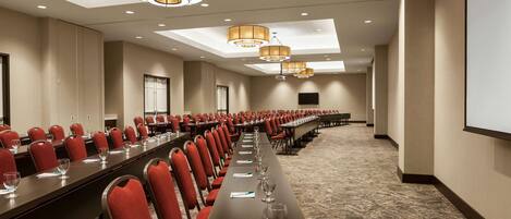 A conference room with rows of red chairs, a long table, and a projector screen.