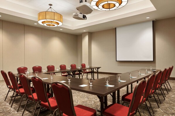 Une salle de conférence avec une longue table, des chaises rouges, un projecteur et un écran.