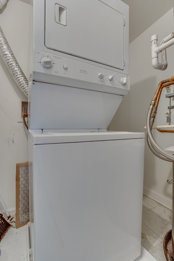A stacked washer and dryer unit in a room with tiled flooring and a visible vent hose. - Heaven on Baltimore Harborfront Fully Furnished Apartments (Baltimore)