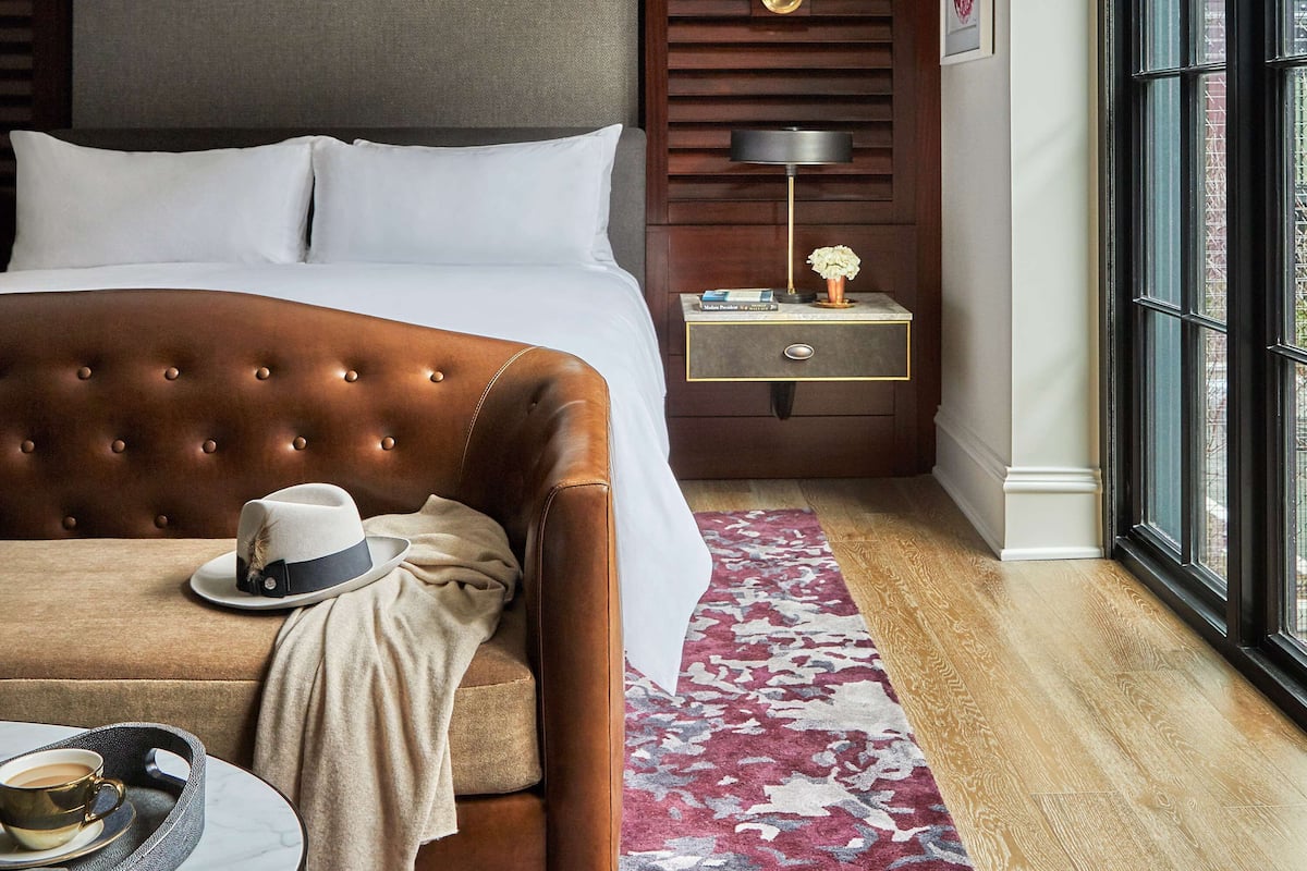 A hotel room with a large bed, a nightstand, a lamp, a window, and a view of the outside.