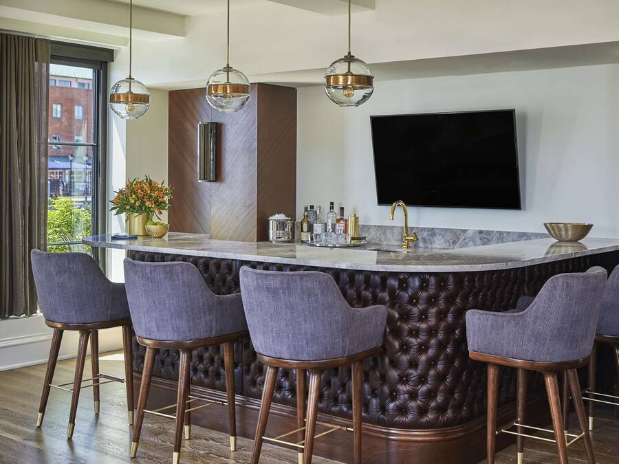 Una cocina moderna con barra, taburetes, un televisor grande y un ventanal con cortinas.