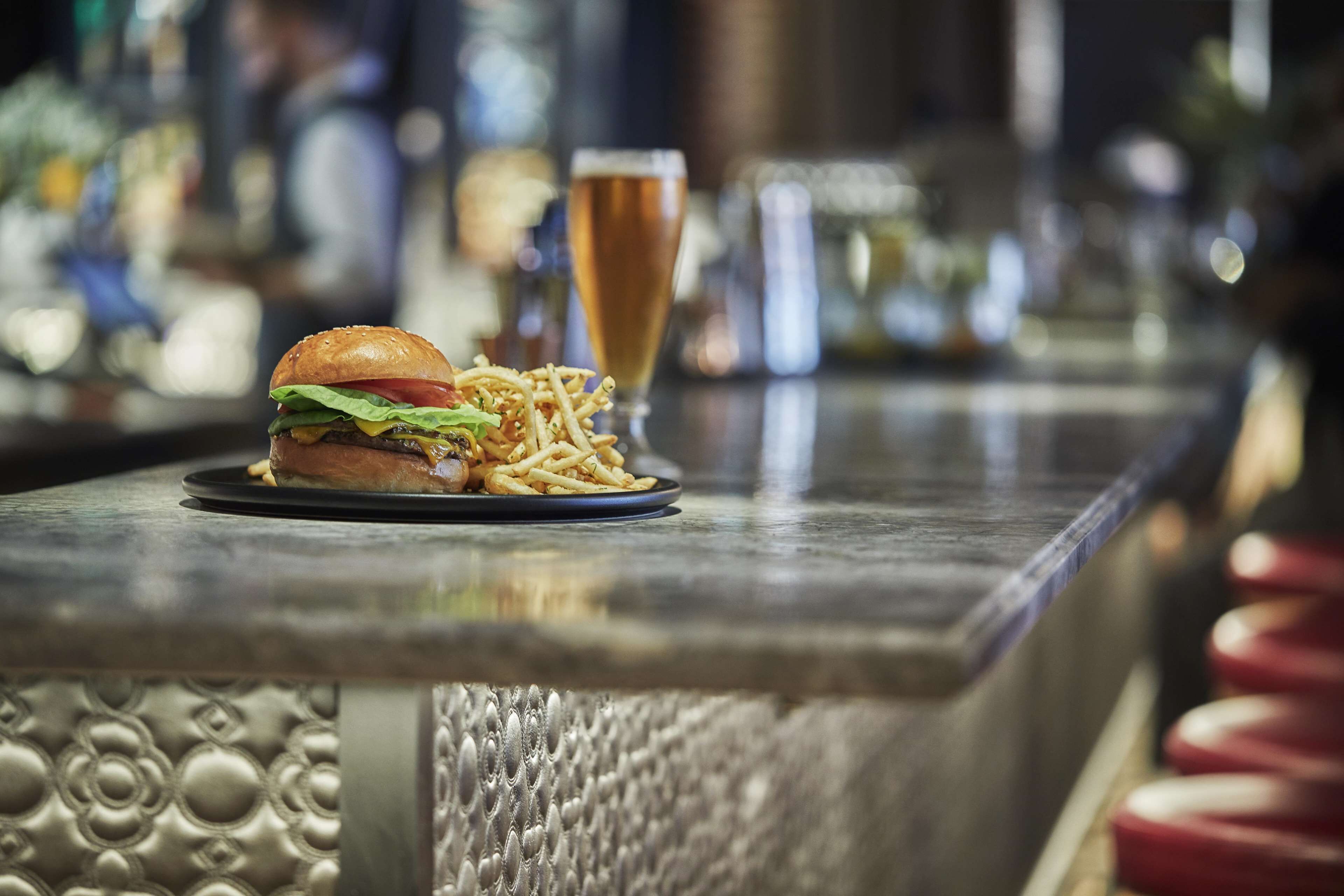 A burger with fries and a glass of beer on a bar counter.