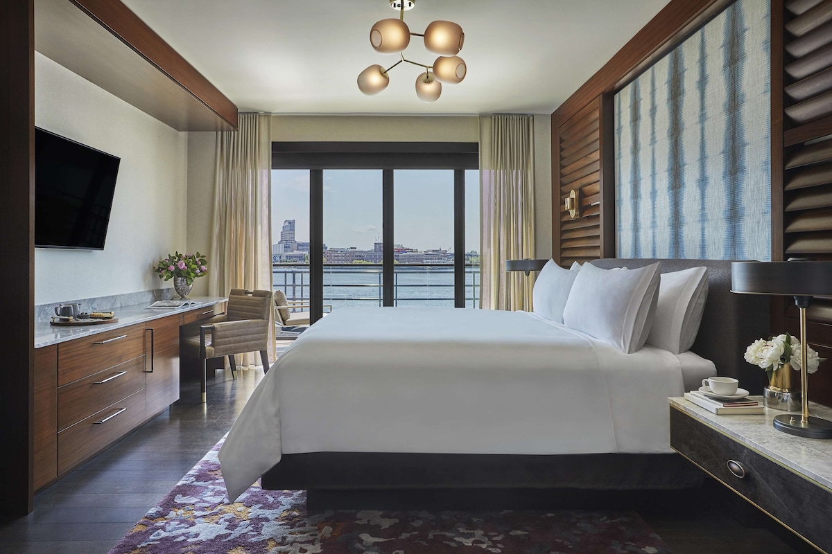 Une chambre d’hôtel avec un grand lit, un bureau, une télévision et une vue sur le paysage urbain, grâce à de grandes fenêtres.