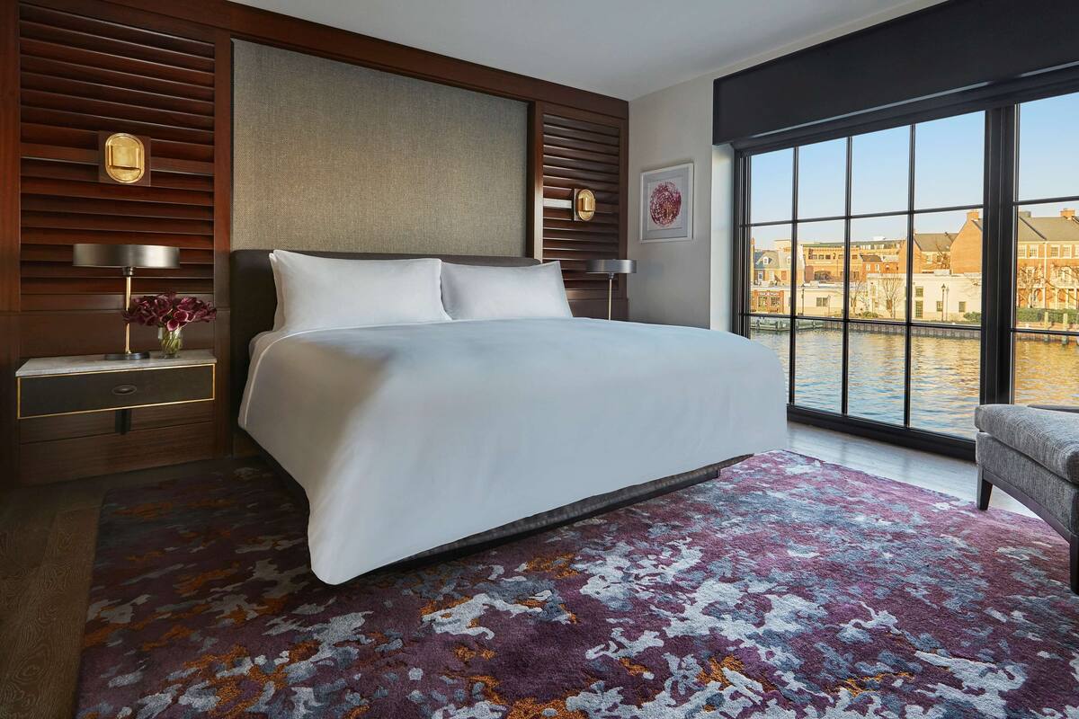 A modern hotel room with a large bed, a view of a canal, and a cityscape.