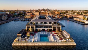 A waterfront hotel with a pool, outdoor seating, and a view of the cityscape.