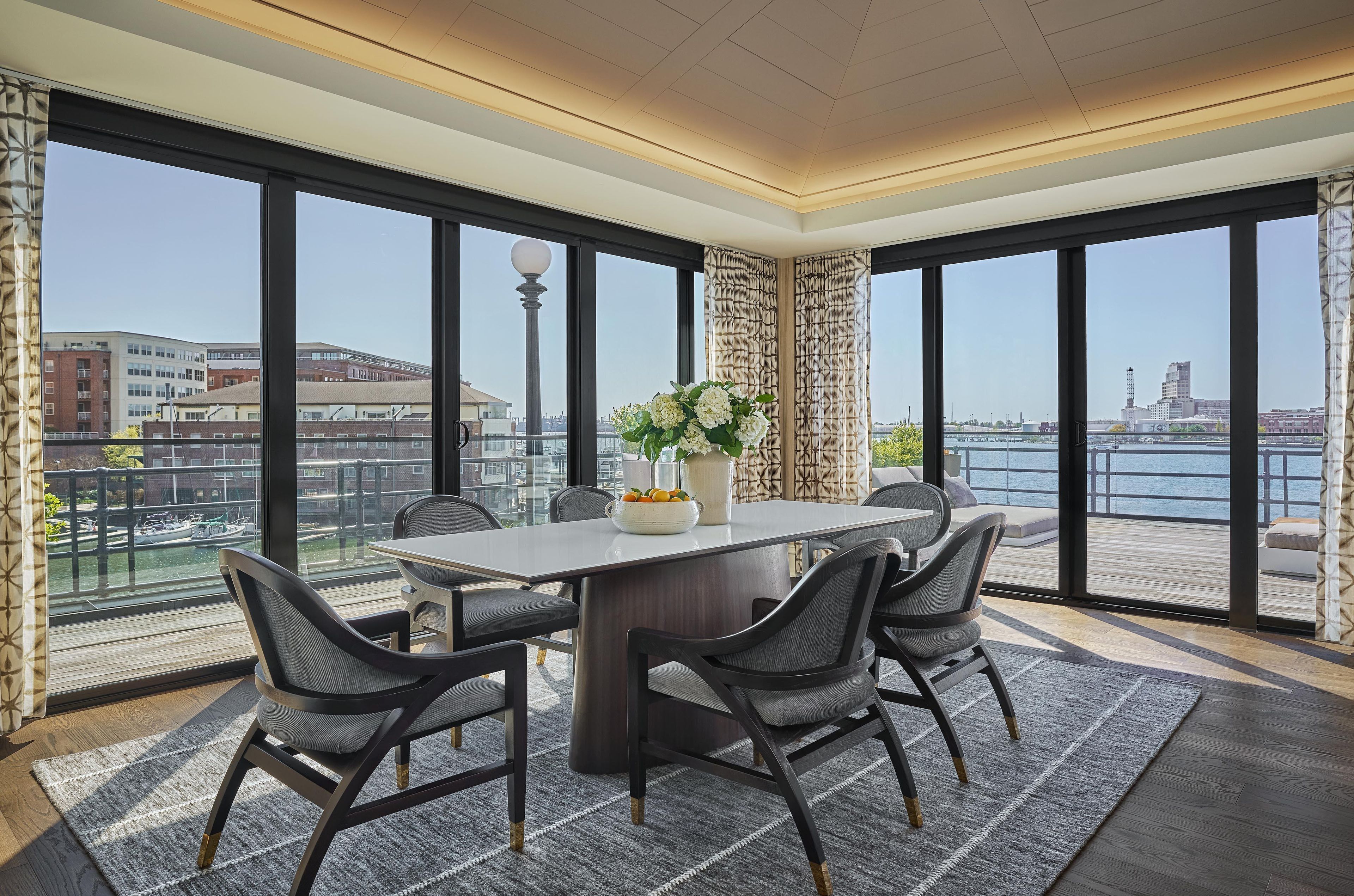 Un comedor moderno con una mesa y sillas, un jarrón con flores y vistas a un paisaje urbano y al agua.