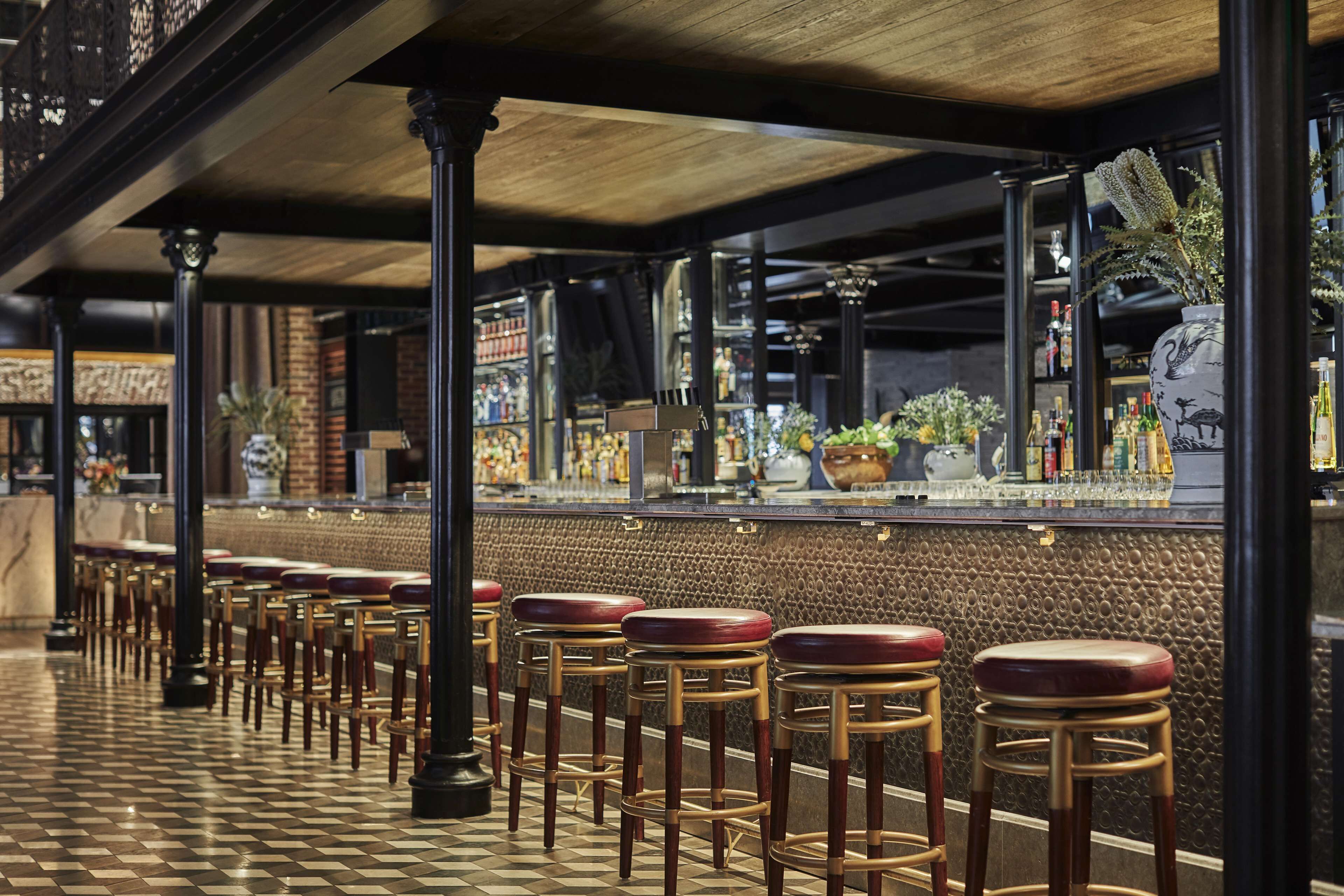 A bar area with a checkered floor, wooden stools, and a bar counter with various bottles and a decorative vase.