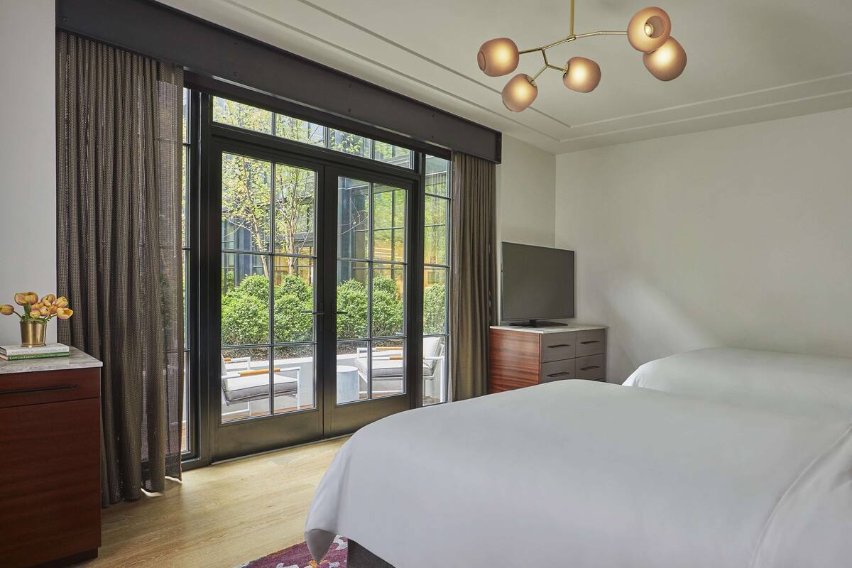 A hotel room with a large bed, a flat-screen TV, a wooden dresser, and a view of greenery through the window.