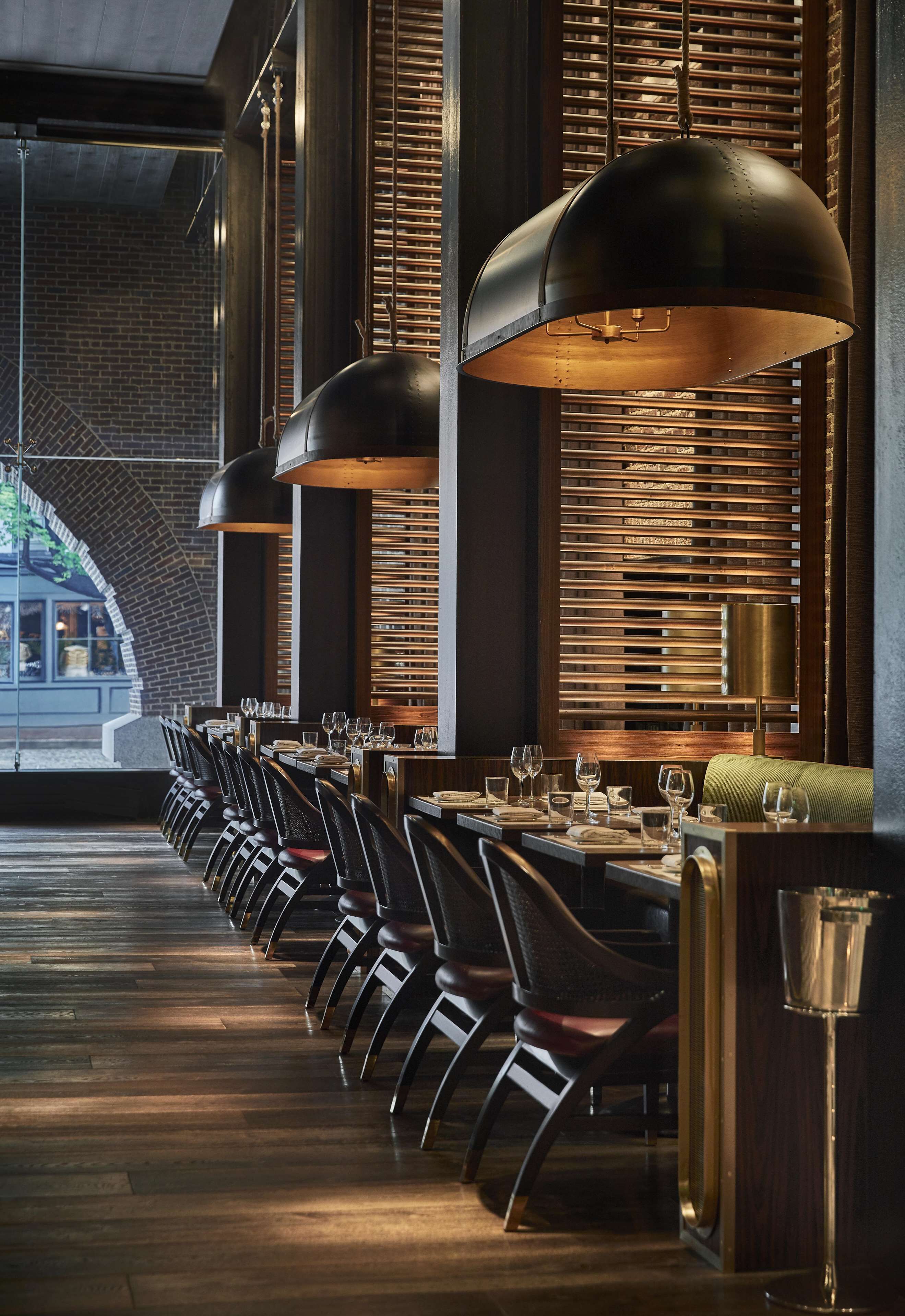 A restaurant with a long counter, black chairs, and large pendant lights.