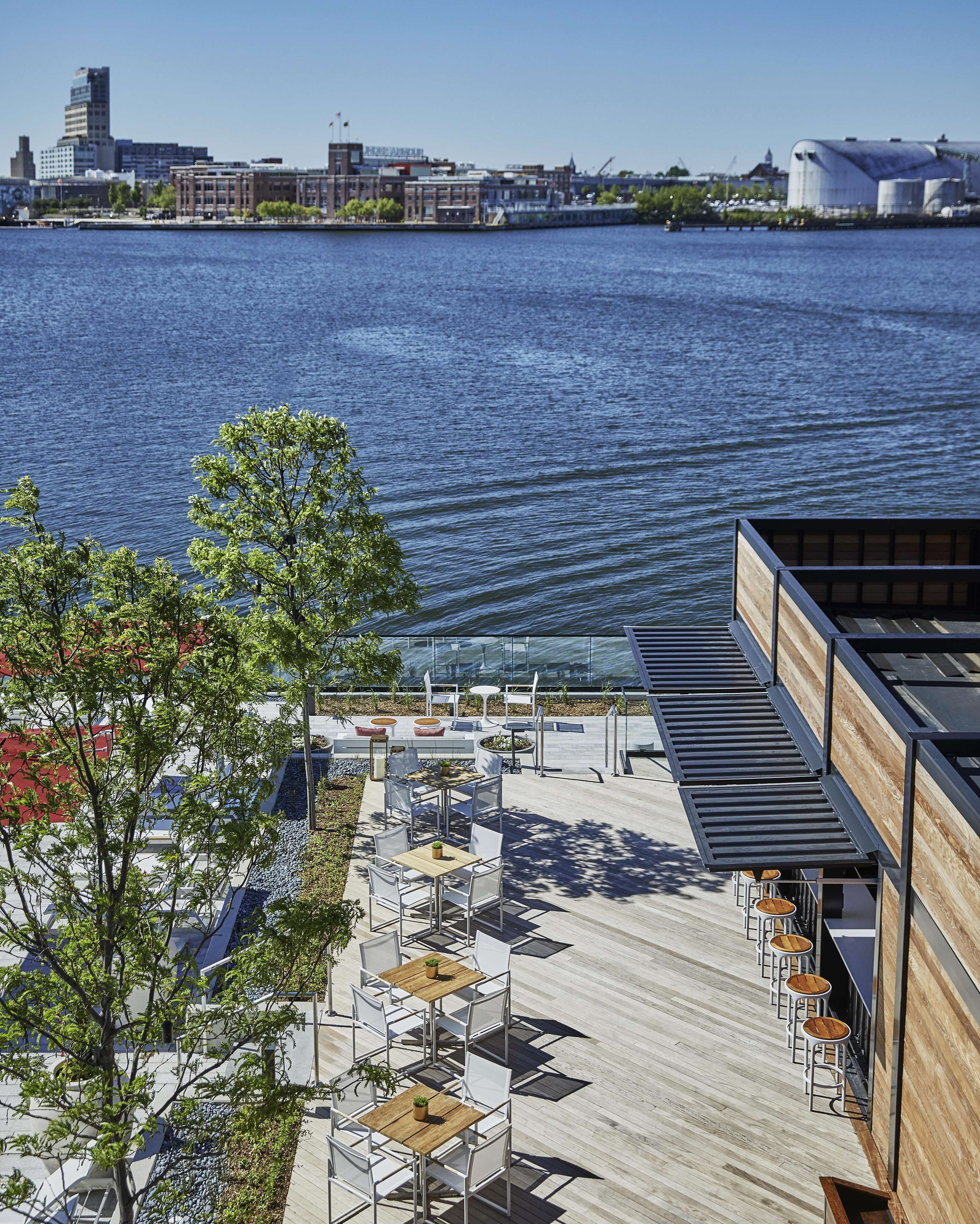 A waterfront patio with outdoor seating, a view of the water, and buildings in the background.
