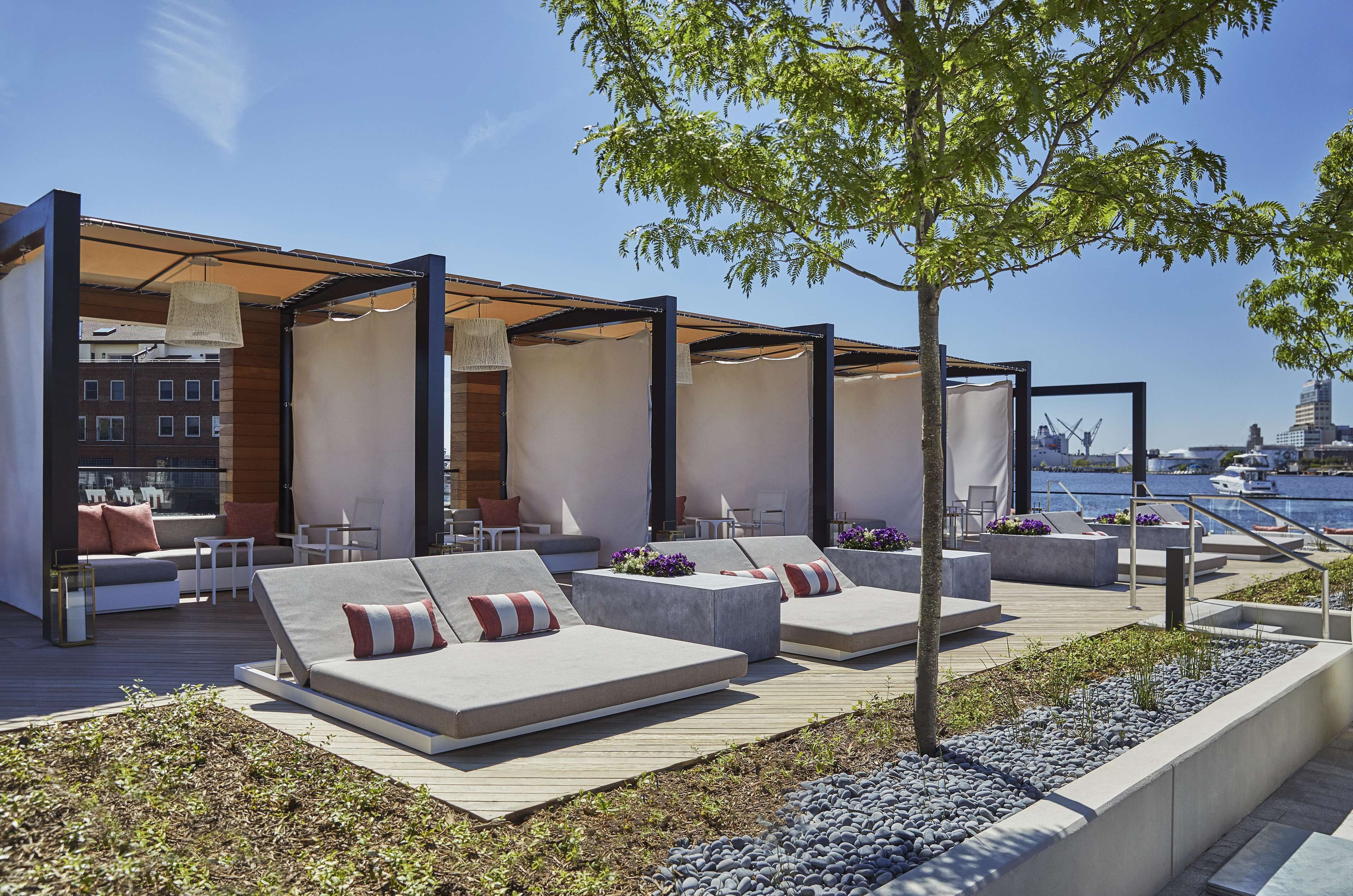 An outdoor seating area with modern furniture, a tree, and a view of the water and buildings in the background.