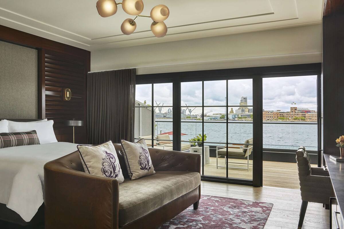 A hotel room with a large bed, a sofa, and a view of the water and cityscape.