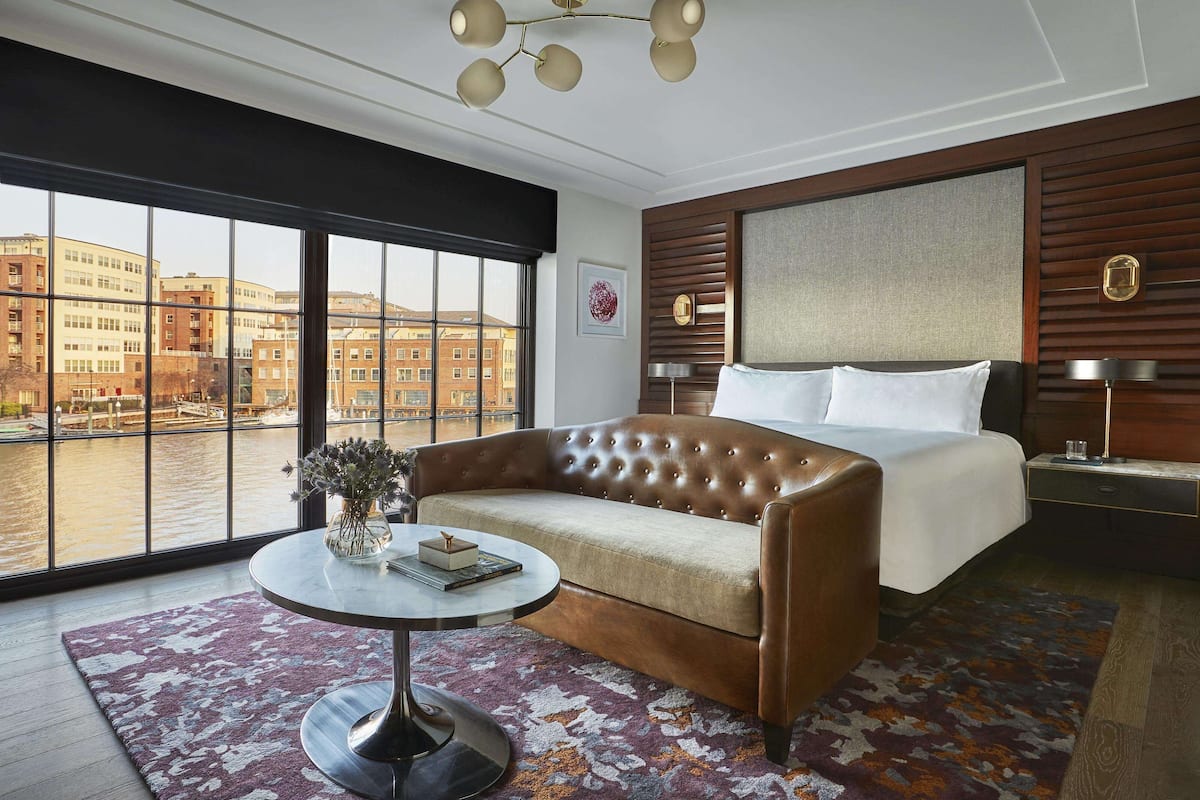 A modern hotel room with a large window, a sofa, a round table, and a bed.