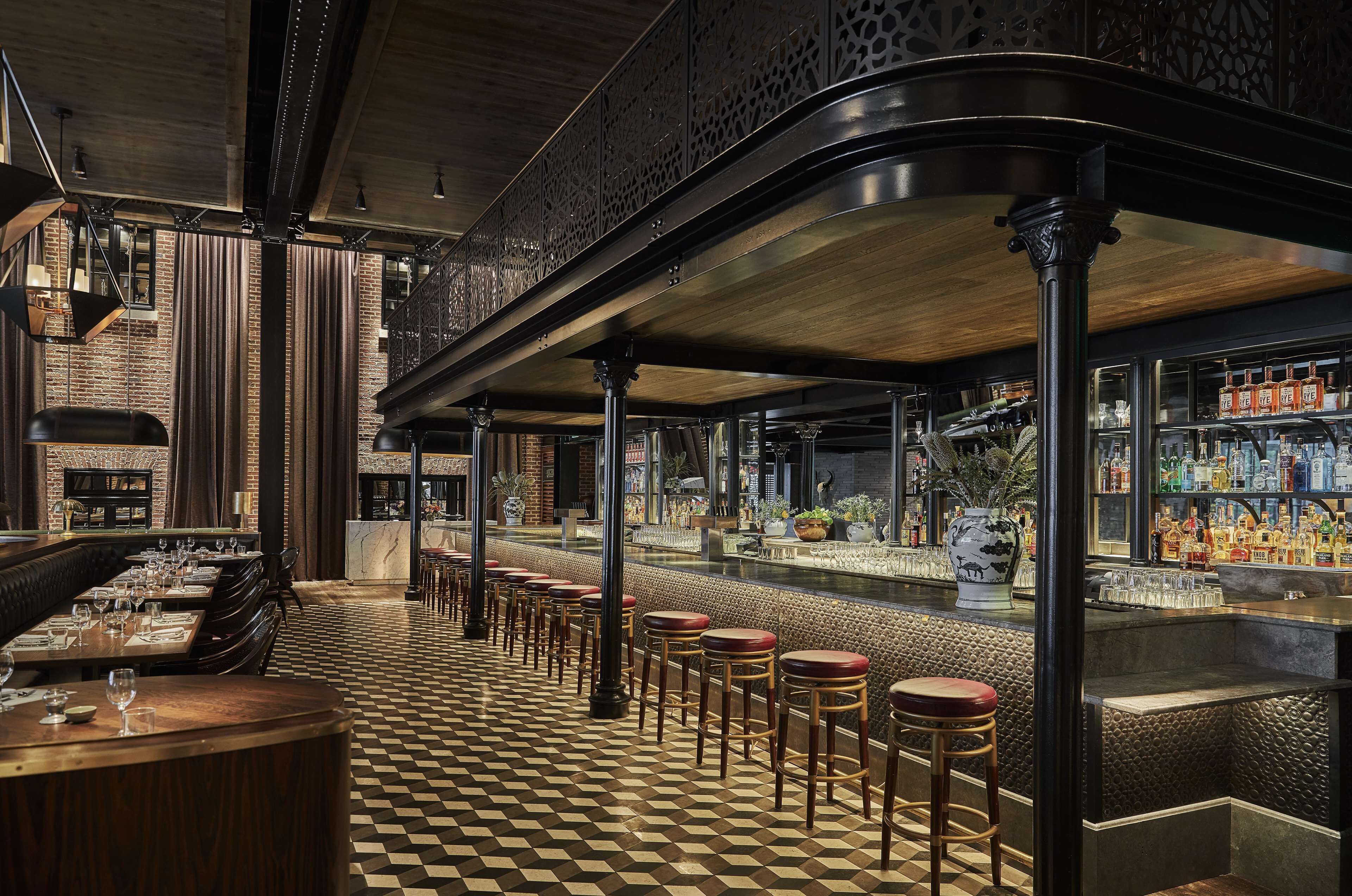 A bar area with a checkered floor, wooden stools, and a bar counter with bottles.