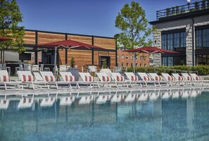 A pool area with lounge chairs and umbrellas, a wooden building, and a stone building with large windows. - Pendry Baltimore (Baltimore)