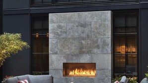 A modern outdoor seating area with a built-in fireplace, two grey sofas, and a round table with drinks. - Pendry Baltimore (Baltimore)