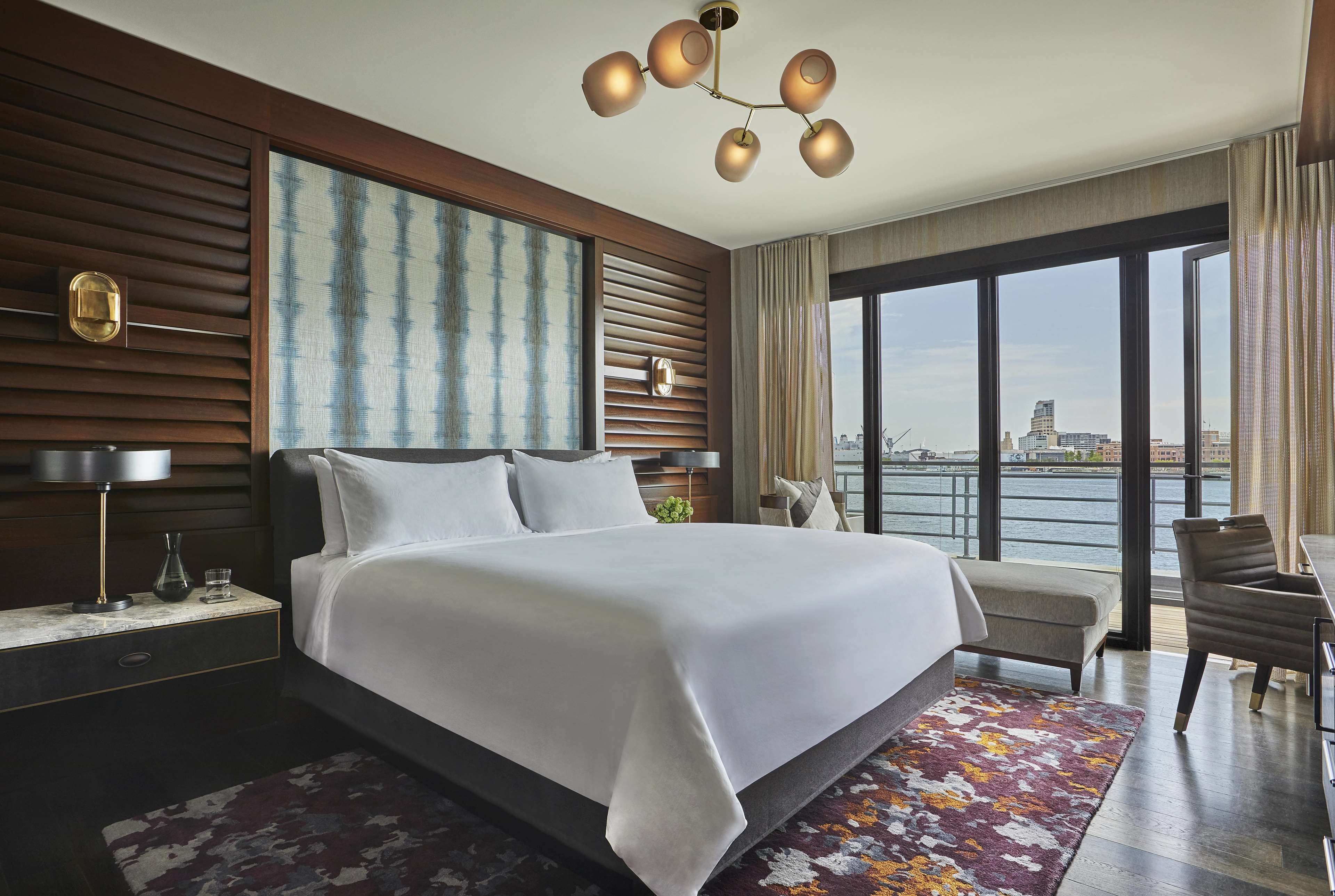 A modern hotel room with a large bed, a view of the city, and a cityscape visible through the windows.