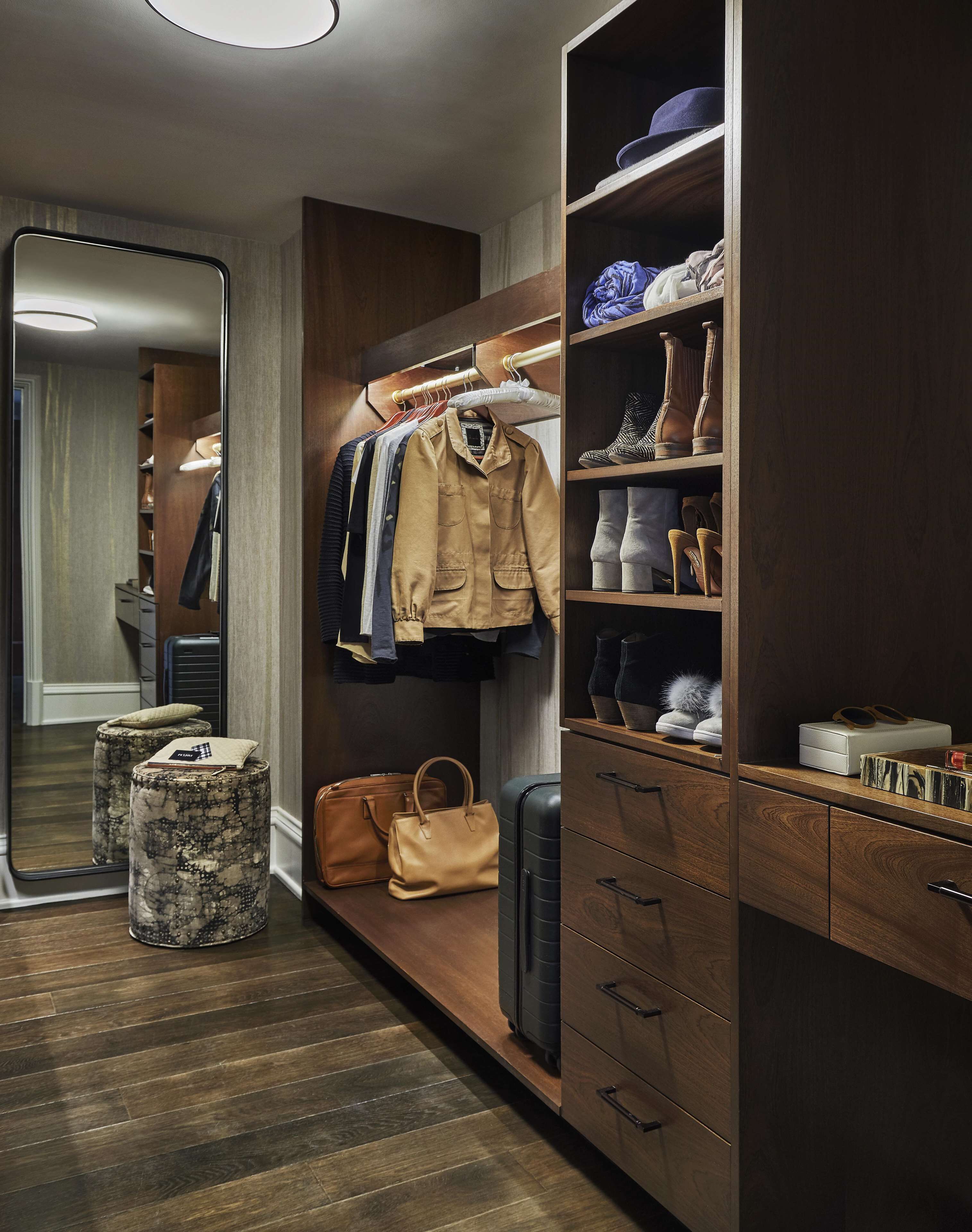 A hotel room with a wooden wardrobe, a mirror, a bench, and a suitcase.