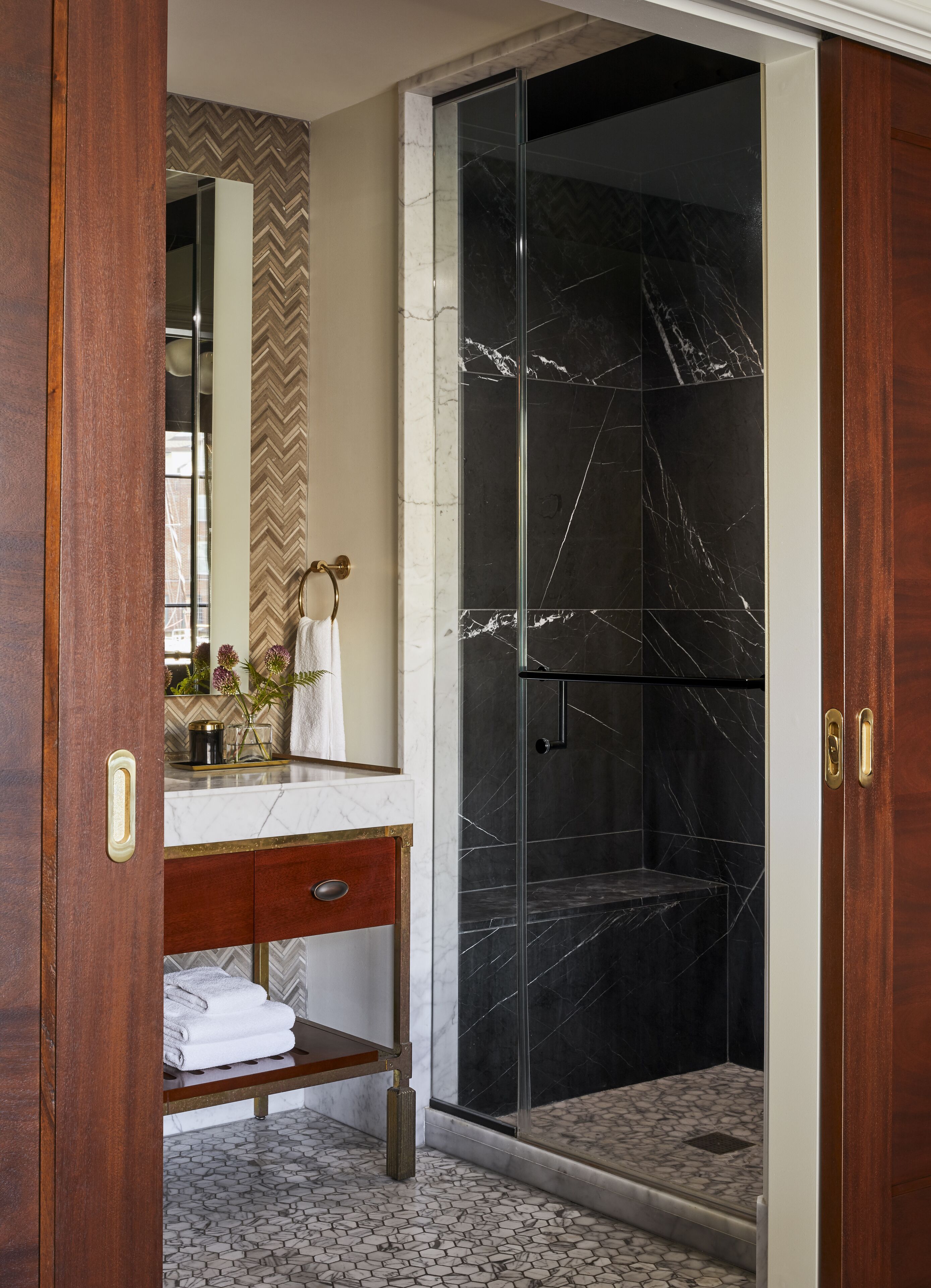 A bathroom with a marble vanity, a glass shower enclosure, and a herringbone-patterned wall.