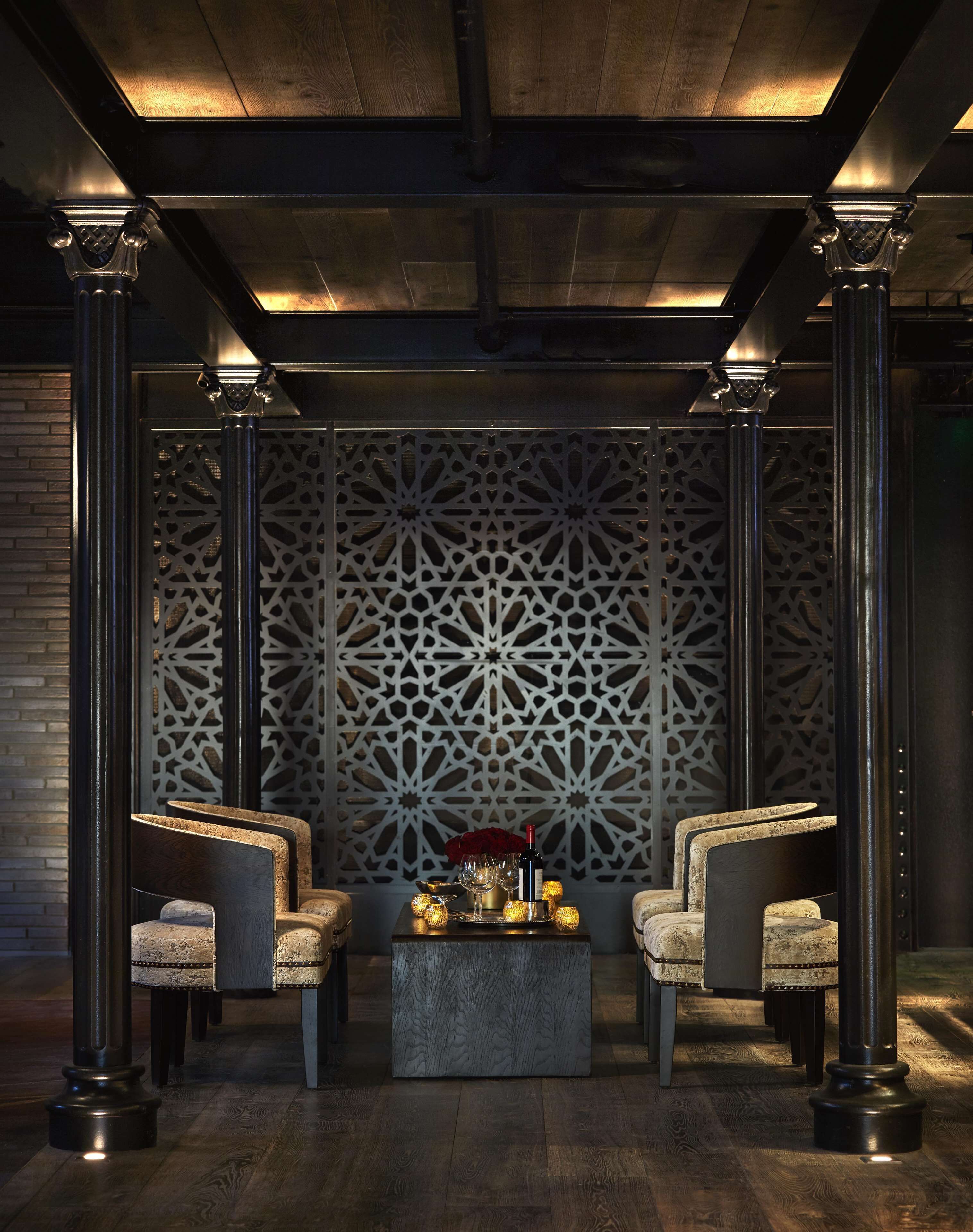 A lobby with a patterned wall, two armchairs, a coffee table with drinks, and a decorative centerpiece.