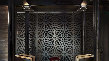 A lobby with a patterned wall, two armchairs, a coffee table with drinks, and a decorative centerpiece.
