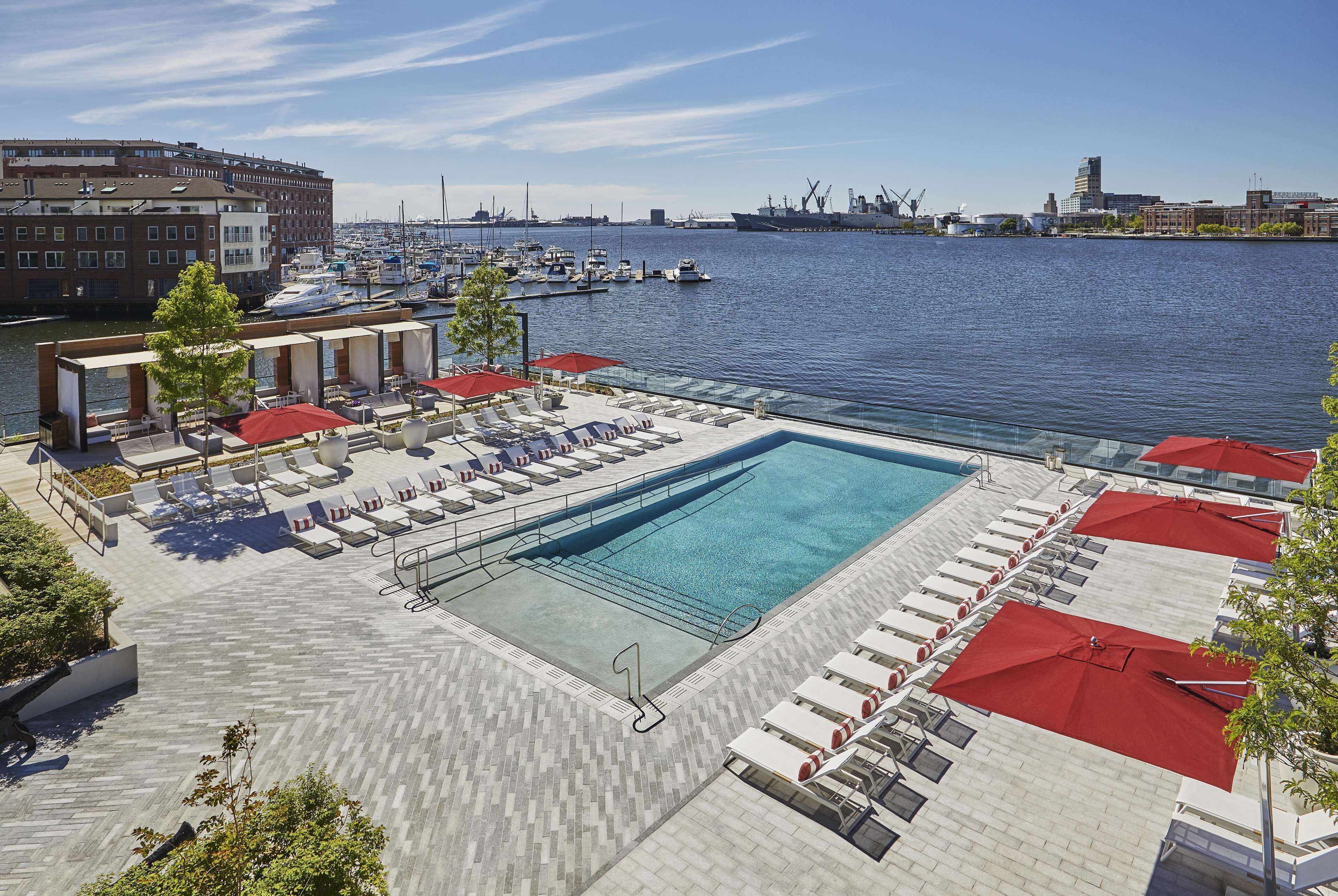 A rooftop pool area with lounge chairs and umbrellas, overlooking a marina with boats and industrial buildings.