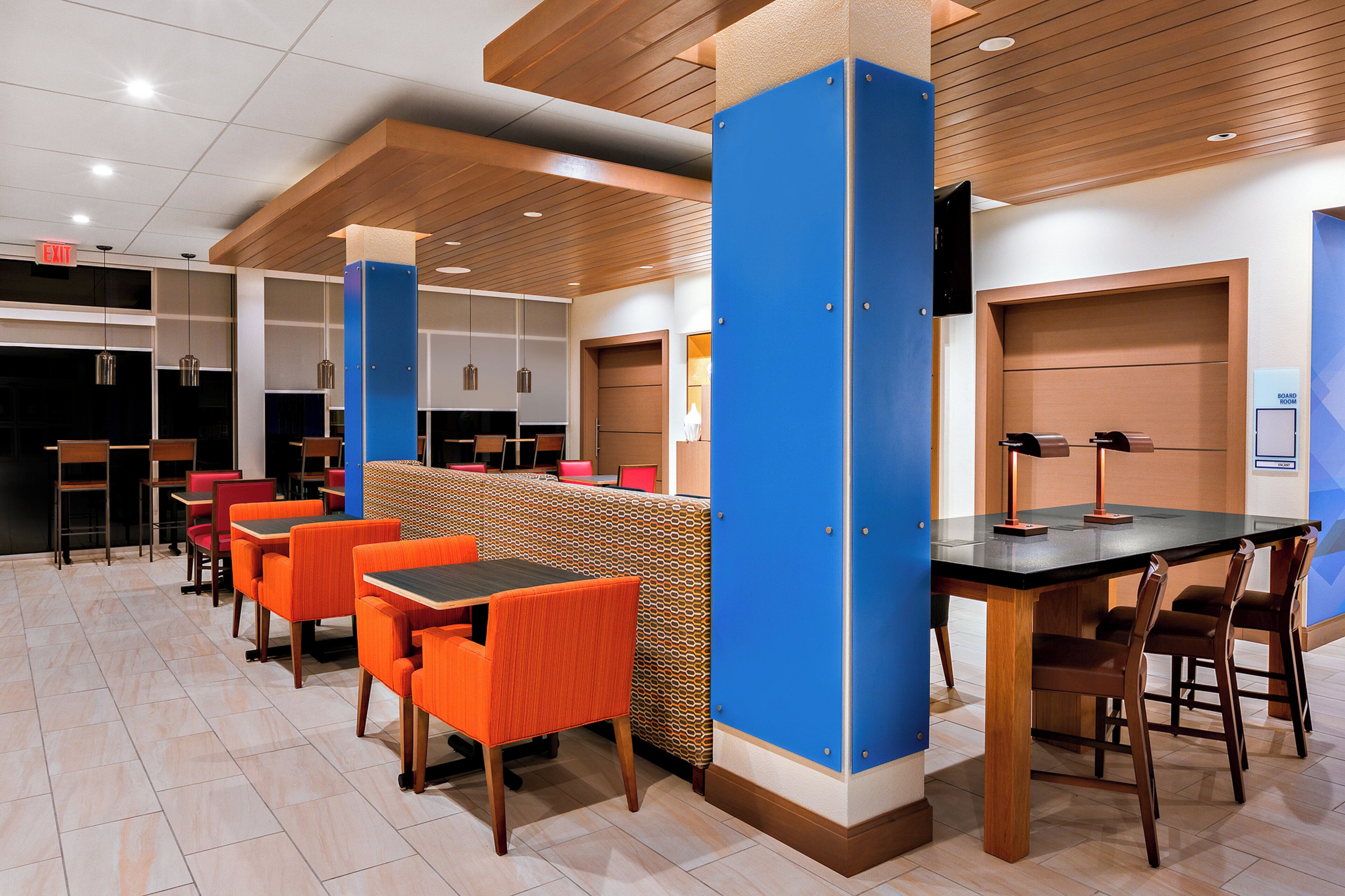 Un intérieur moderne avec un bar, des sièges dotés de chaises orange et un mur d’accent bleu.