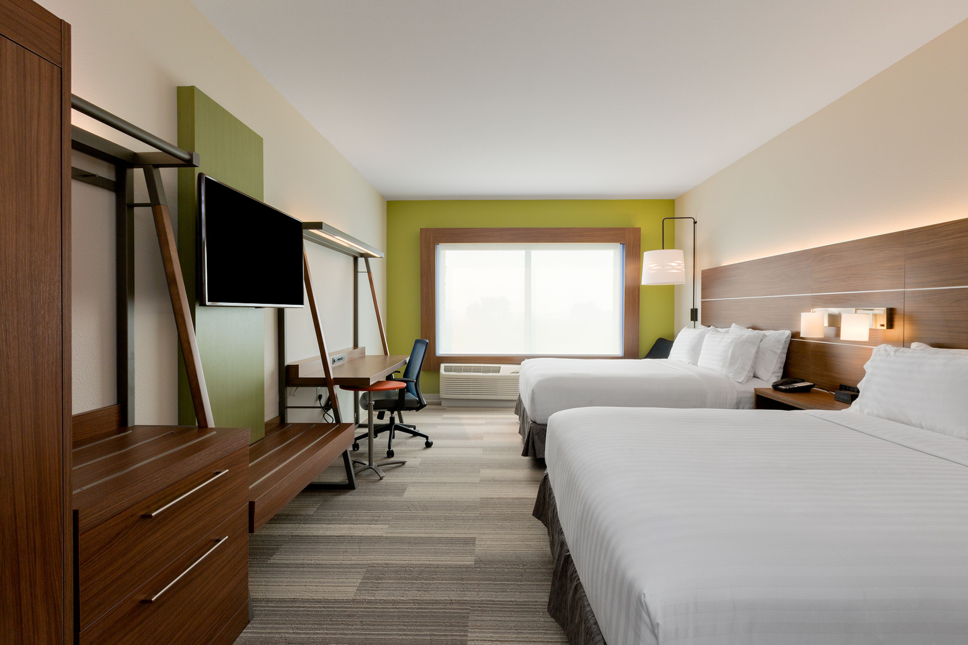 Quarto de hotel com duas camas, uma escrivaninha, uma televisão e uma janela.