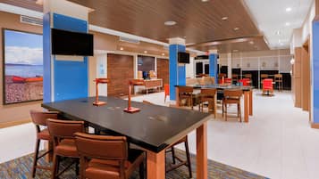 A hotel room with a large flat-screen TV, a wooden ceiling, and a seating area with chairs and a table.