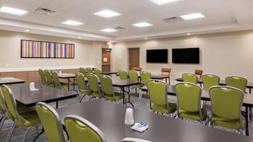 A conference room with tables and chairs, a colorful artwork on the wall, and a flat-screen TV.