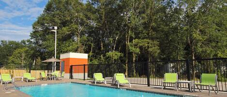 Une piscine entourée d’arbres, avec des chaises longues et un petit pavillon.